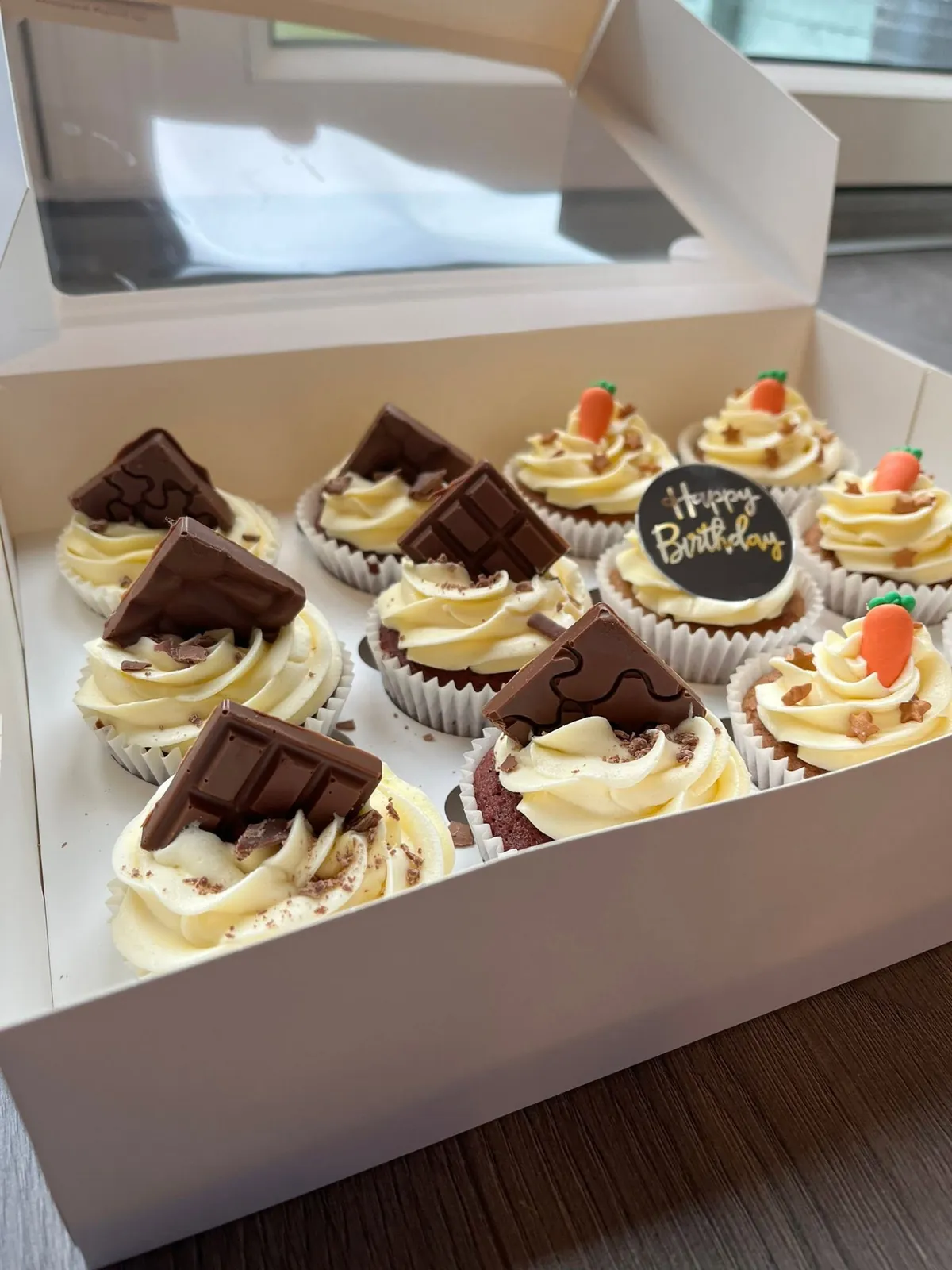 A box of custom cupcakes topped with chocolate and fondant carrots